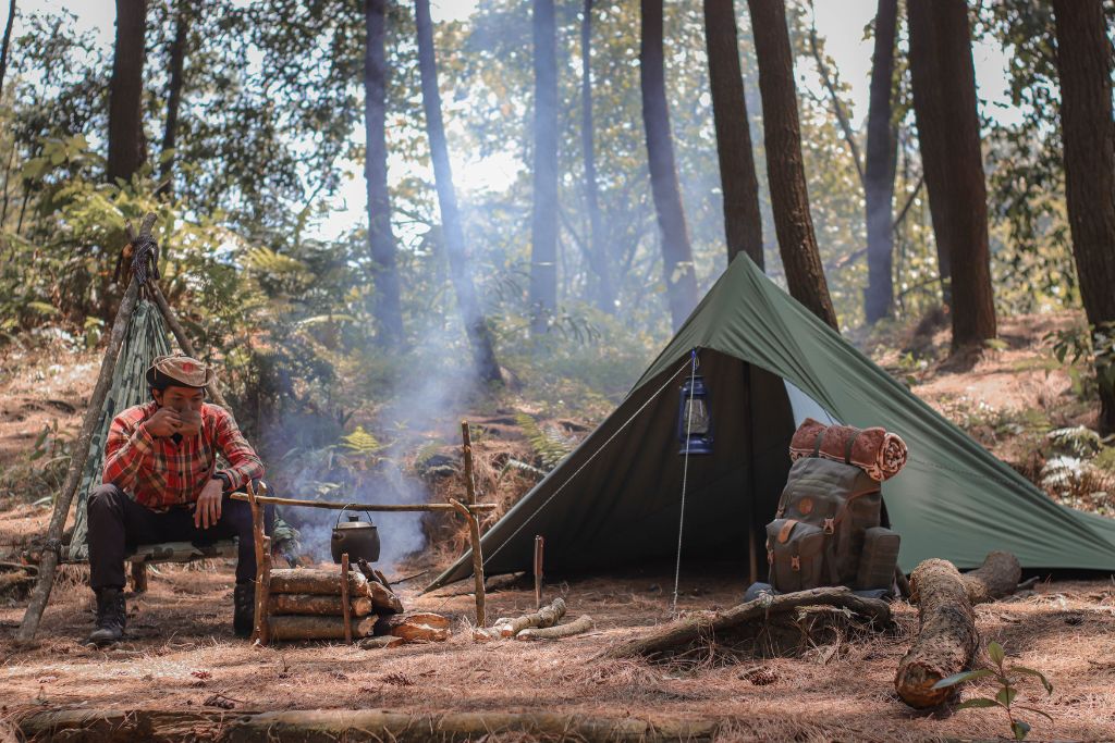 A man is resting at the camp site while drinking on a cup