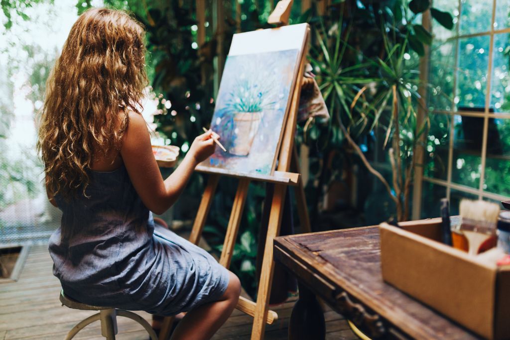 A curly-haired woman doing her painting inside a room full of plants