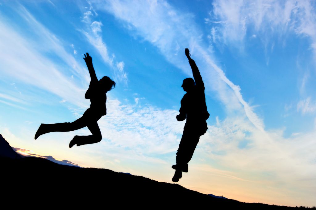 A silhouette of two people jumping above the ground