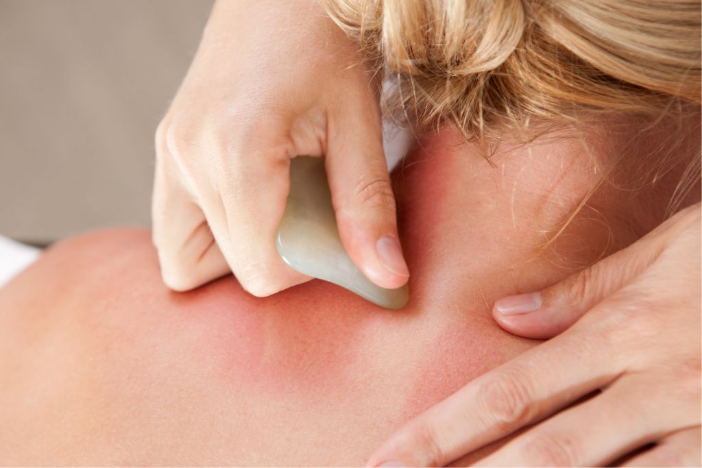 A gua sha stone being massaged at the back area of a woman's neck.