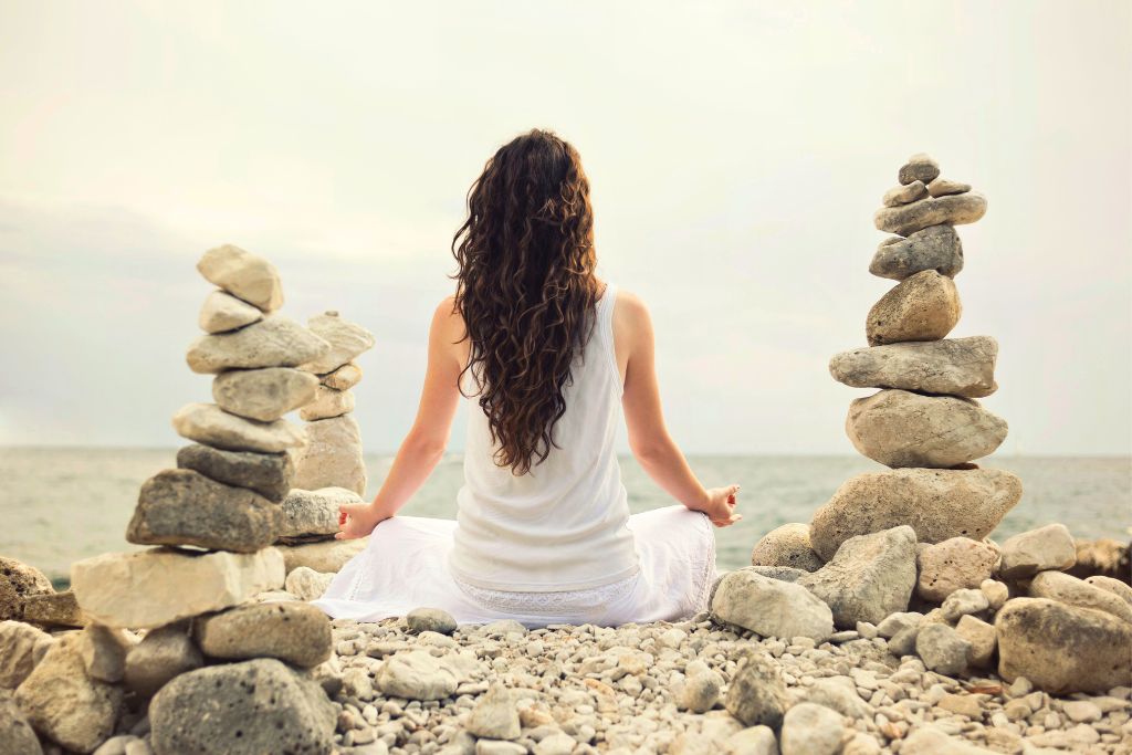 Woman sitting in the seashore surrounded by stacks of rocks