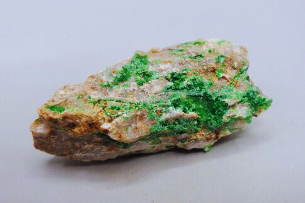 a Conichalcite stone placed on a clear space and has a graysihwhite paint on the background. Image source: Etsy | Dereck HealingCrystalShopCA