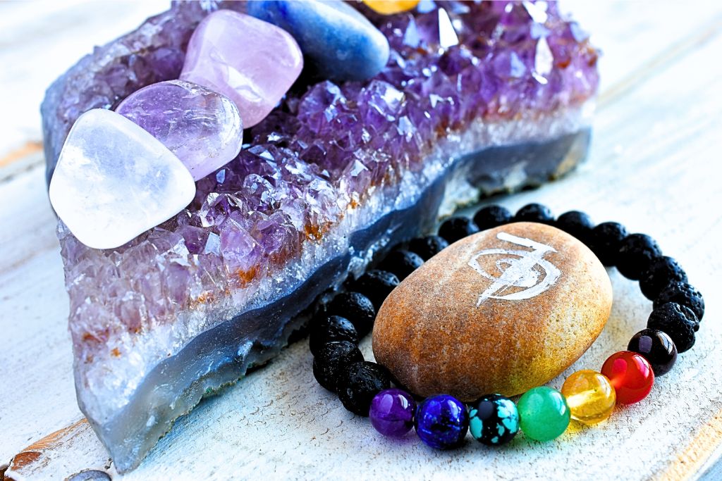 a crystal bracelet beside an amethyst geode and other tumbled crystal