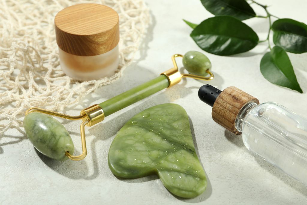 Jade roller, Jade gua sha stone, a bottle of essential oil and a cream 