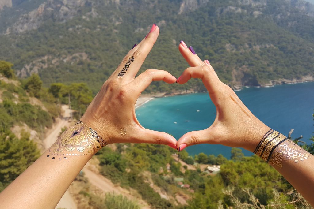 two hands formed a heart sign with a beautiful ocean and trees scenery in the background