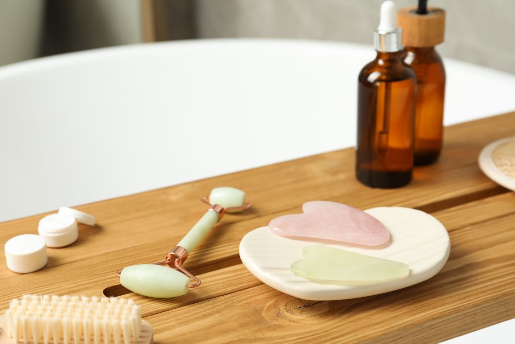 Jade and Rose Quartz Gua Sha Stones in a plate beside a jade roller and a oils