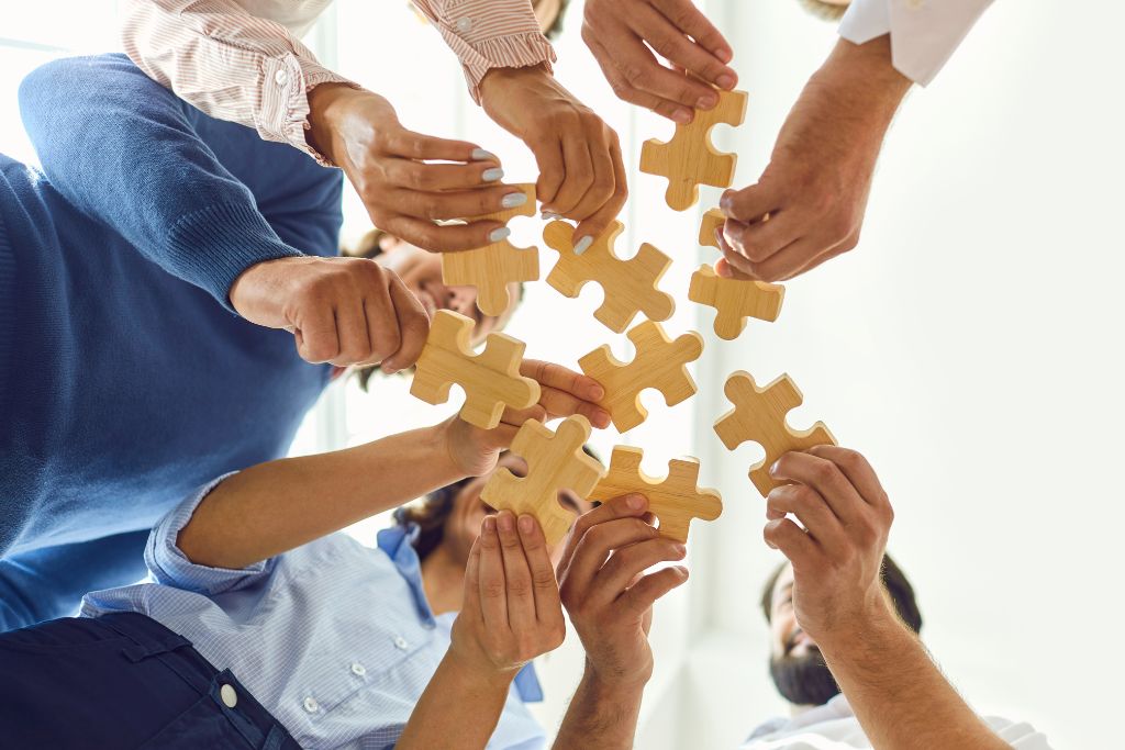 Coworkers are joining parts of a jigsaw puzzle together for it to be interconnected