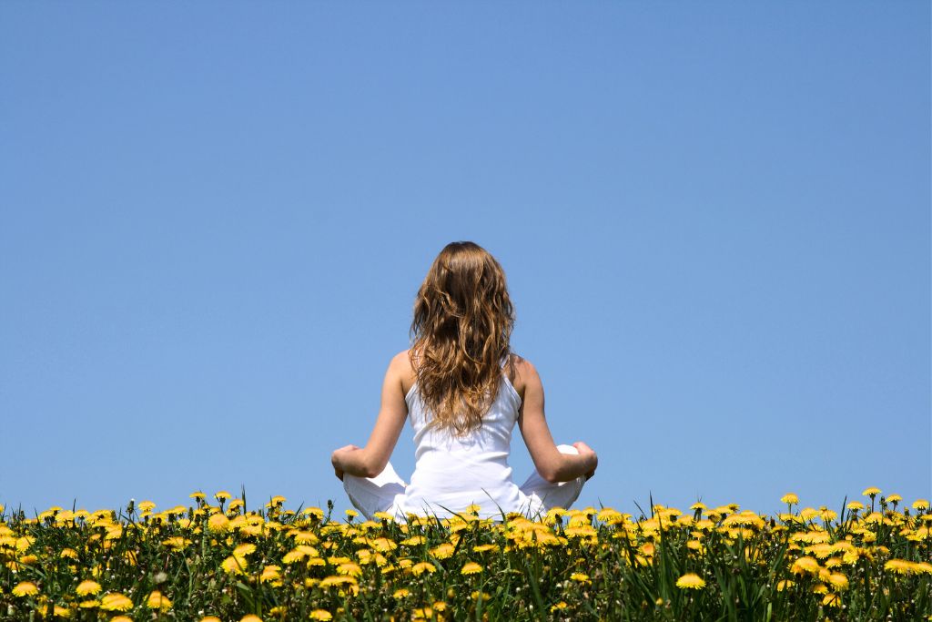 woman meditating in an outdoor setting and surrounded by yellow flowers