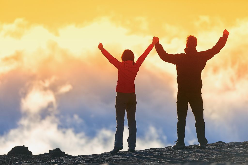 A man and woman are holding each other hands while raising them on a cliff