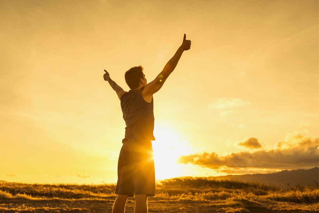 man feeling protected and raising his hands in the air under sunrise