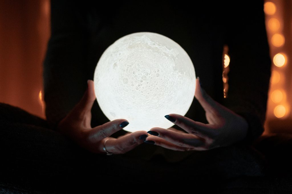 A person holding a glowing crystal ball that looks a moon