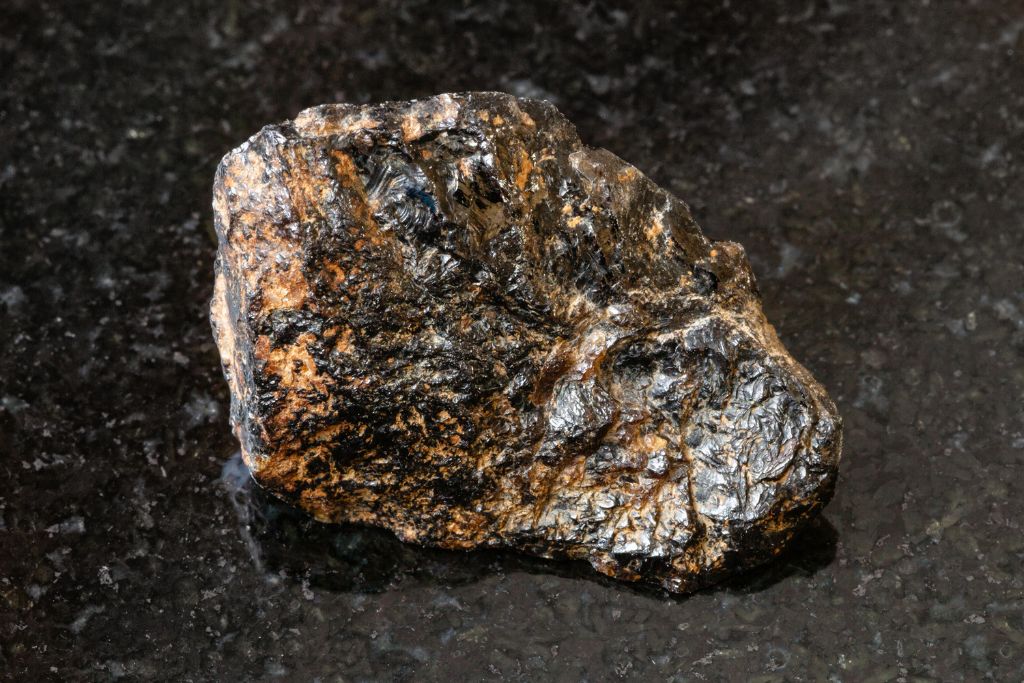 A raw Cassiterite crystal on a black granite