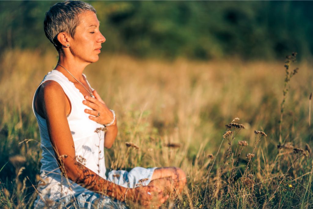 The woman is meditating in a field surrounded by grass.