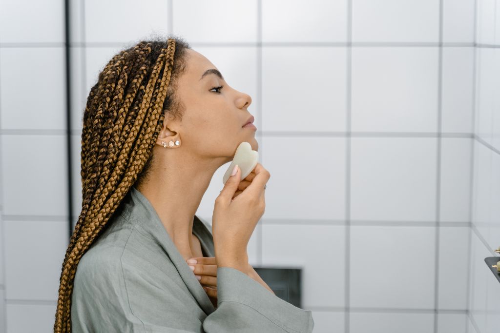 Woman in grey long sleeve shirt doing a gua sha massage in a bathroom