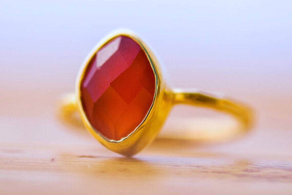 A ring made of carnelian with a gold band is placed on a table.