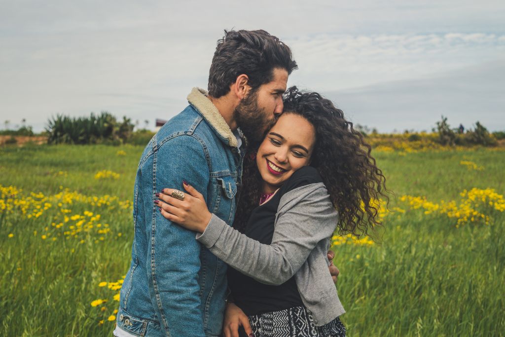 a man kissing a woman in the head with grass and flowers around them