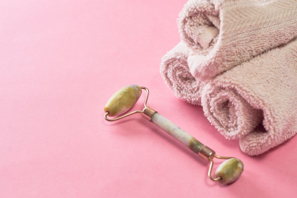 A crystal face roller with towels on a pink background