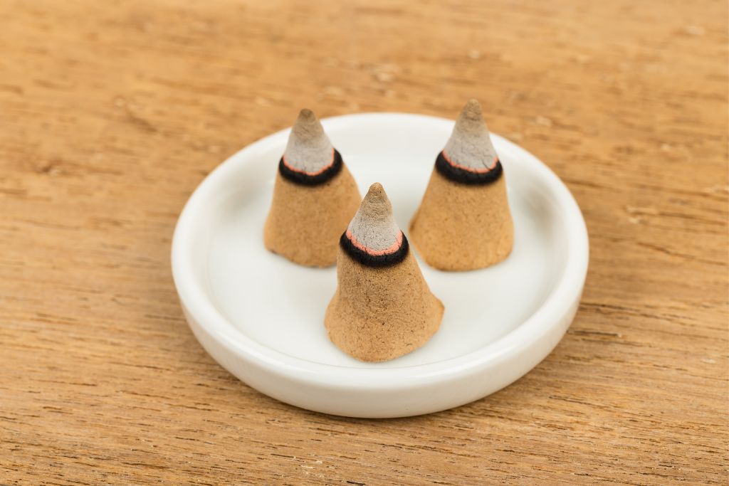 3 burning incense cones on a white dish