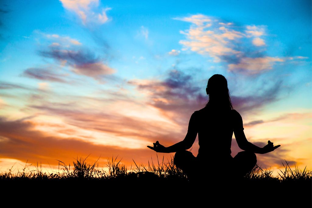 A woman is meditating outside, surrounded by a beautiful sky scenery.