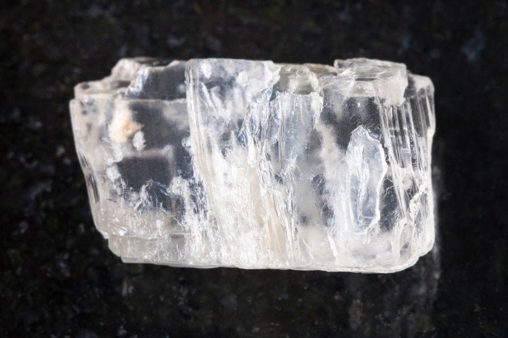 a raw petalite crystal on a black granite