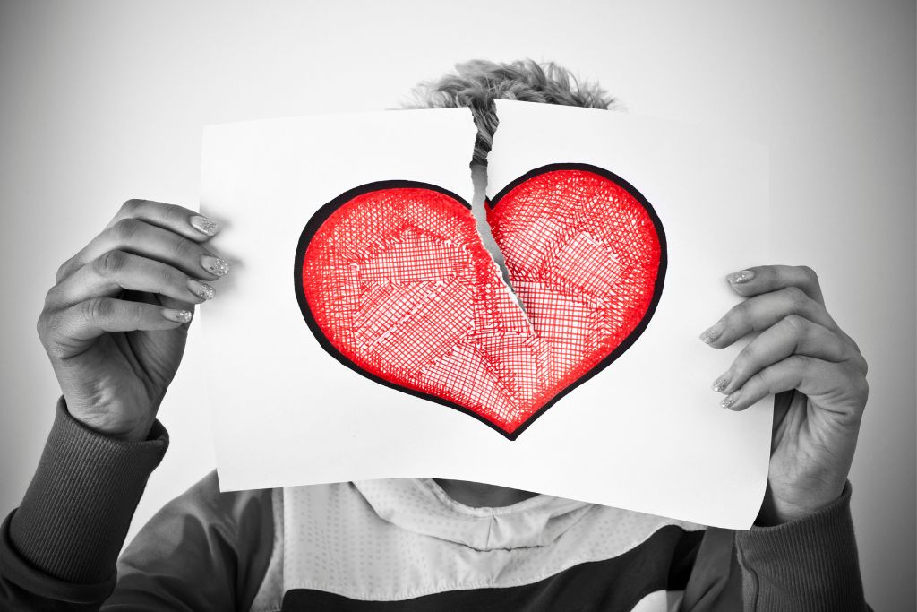 a person tearing a paper with a heart-shaped drawing in half