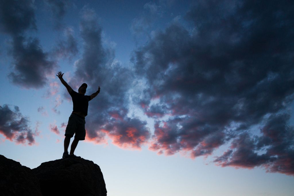 silhouette picture of a man standing on a rock and arms wide open 