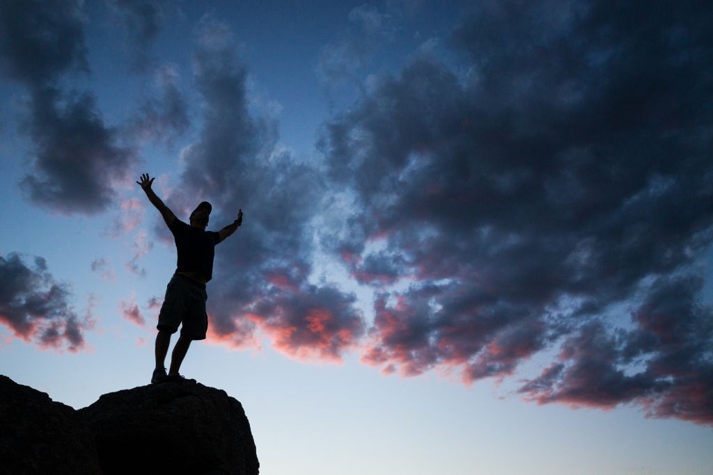 silhouette picture of a man standing on a rock and arms wide open