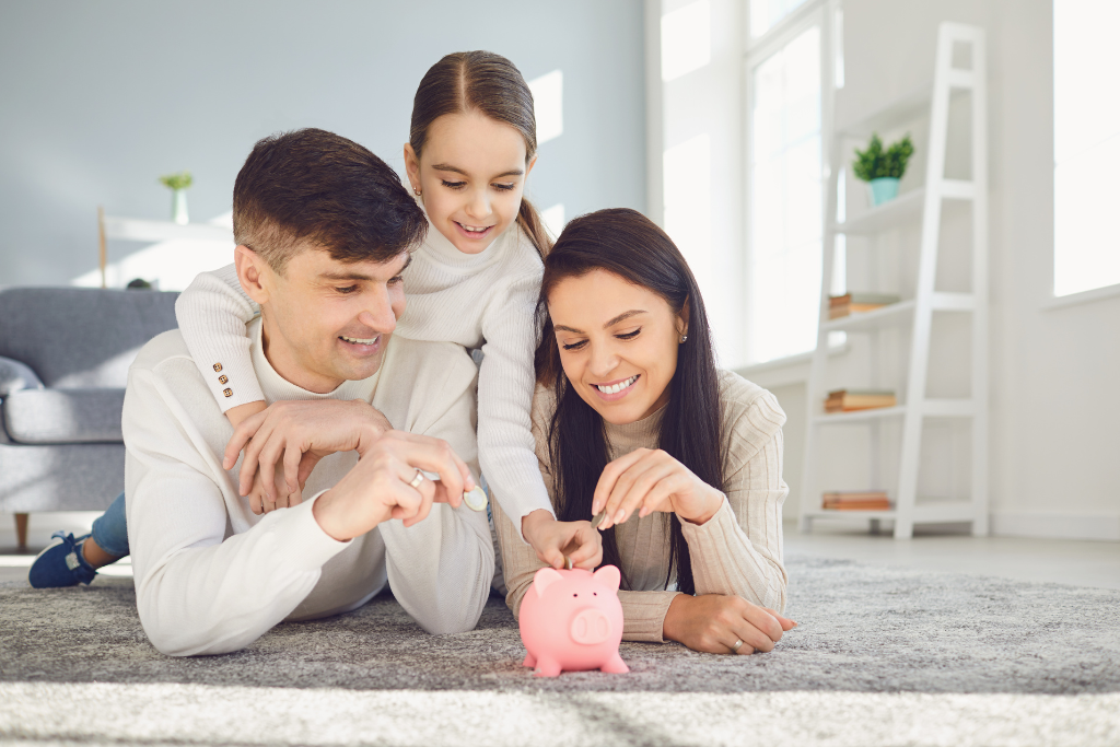 family compose of 1 female child, husband and wife putting coins on piggy bank