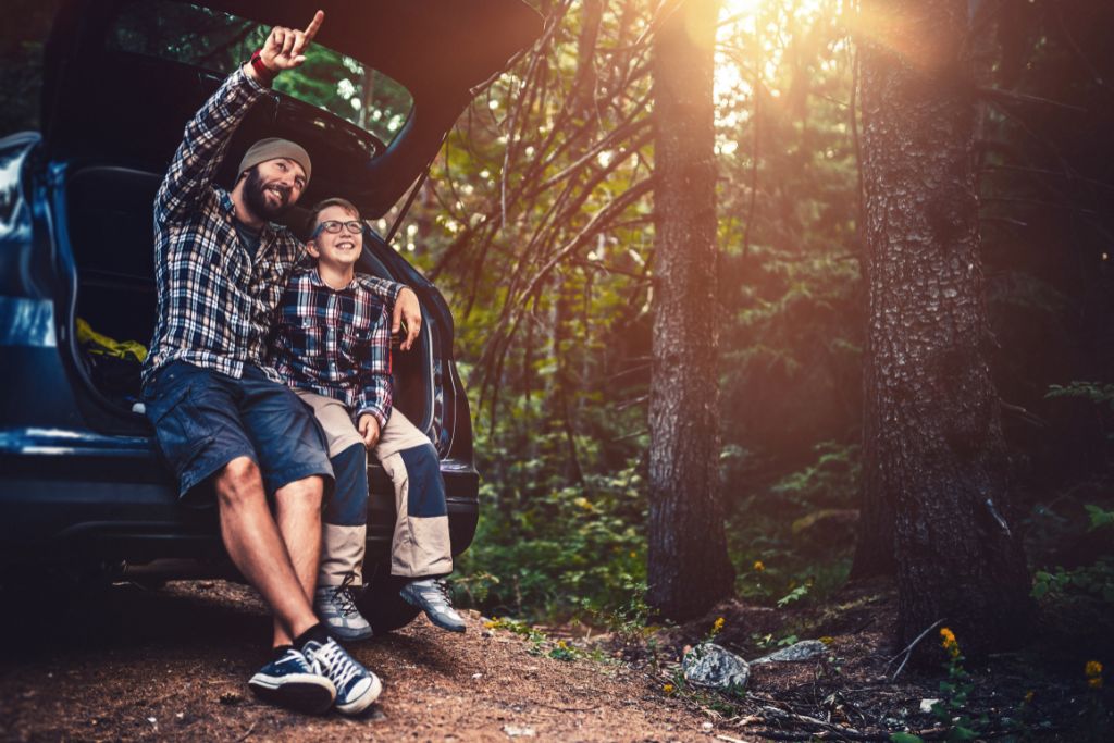 A dad and Son is sitting on the back of the car in nature