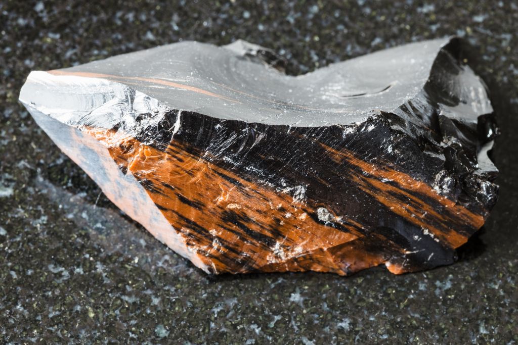 A raw Mahogany Obsidian crystal on a black granite