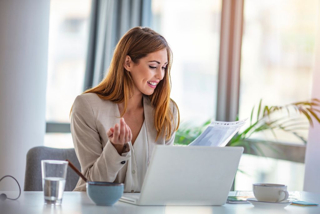 A happy woman holding a piece of paper while in front of her laptop.