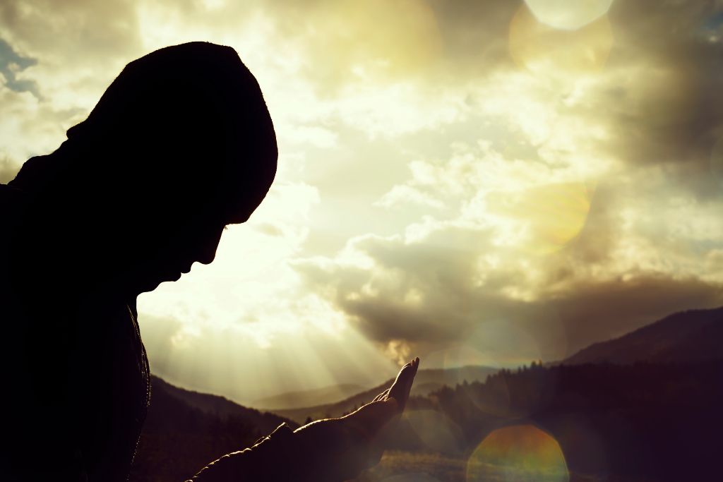 A silhouette of a man facing downward in front of his lifted palm.