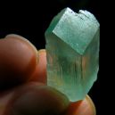 piece of Hiddenite on a finger tip on black background