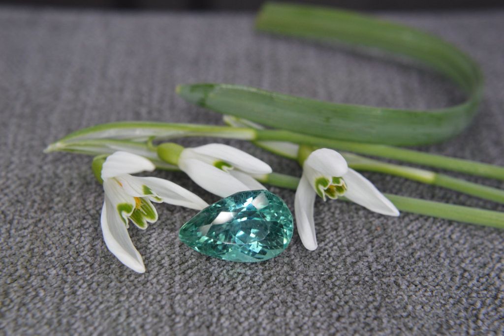Hiddenite behind white flowers on a gray cloth