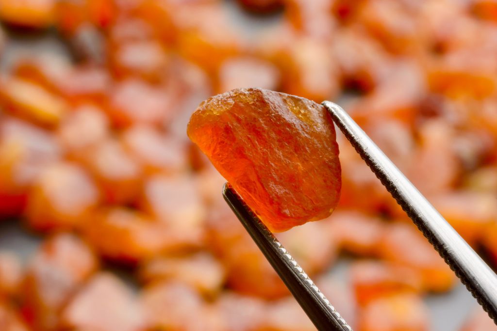 A Spessartite Garnet Crystal is being hold by a tweezer