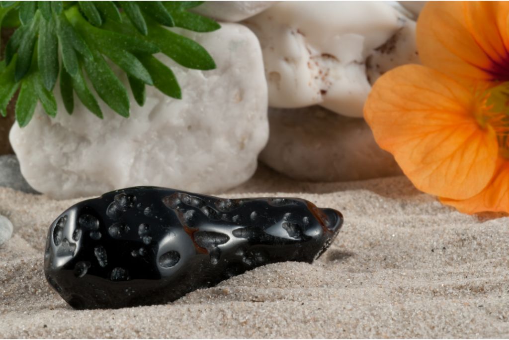 Tektite stone on sand with flowers and stones background.