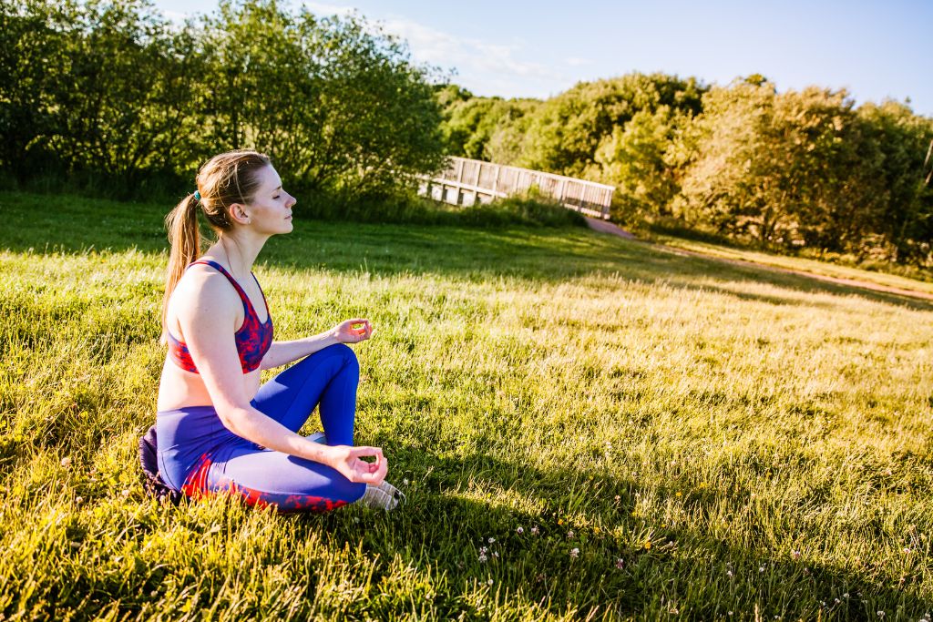 A person meditating outside on a green grass with a basking sun.