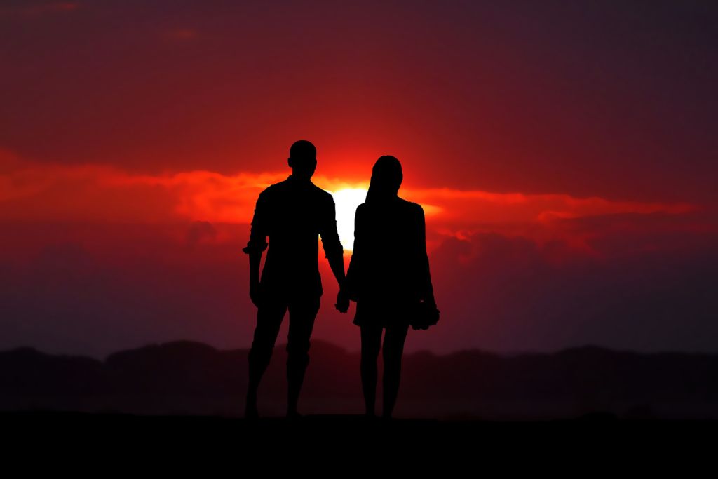 A couple's silhouette by an orange setting sun. 