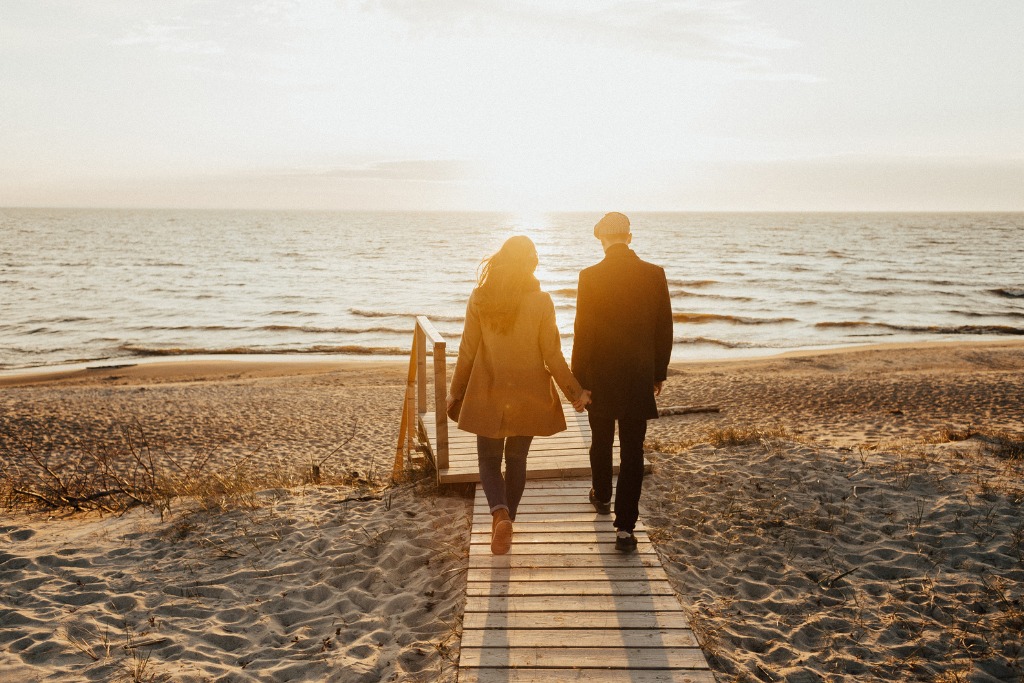 man and woman holding hands walking in a beach