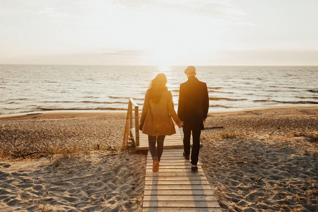 man and woman holding hands walking on the beach