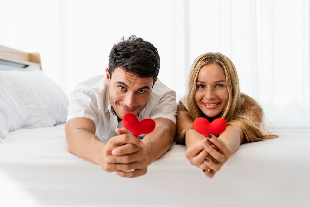 couple lying on the bed holding a small heart shape cushion