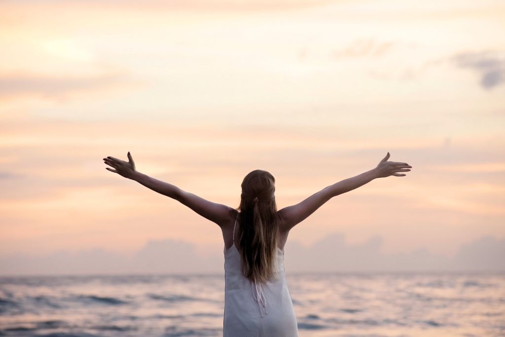 woman spreading her arms openly on a pinkish sunset