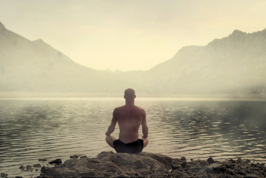man doing meditation in front of a smoky lake