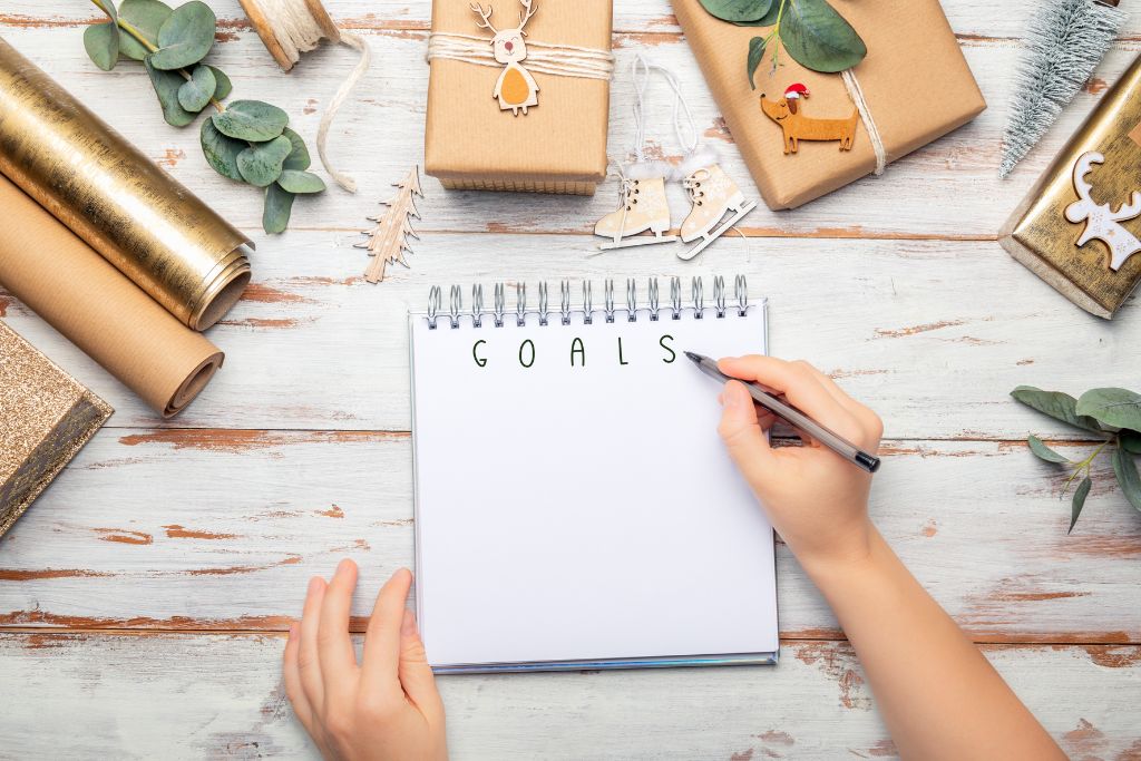 a hand writing goals on a notebook surrounded by wrapped presents