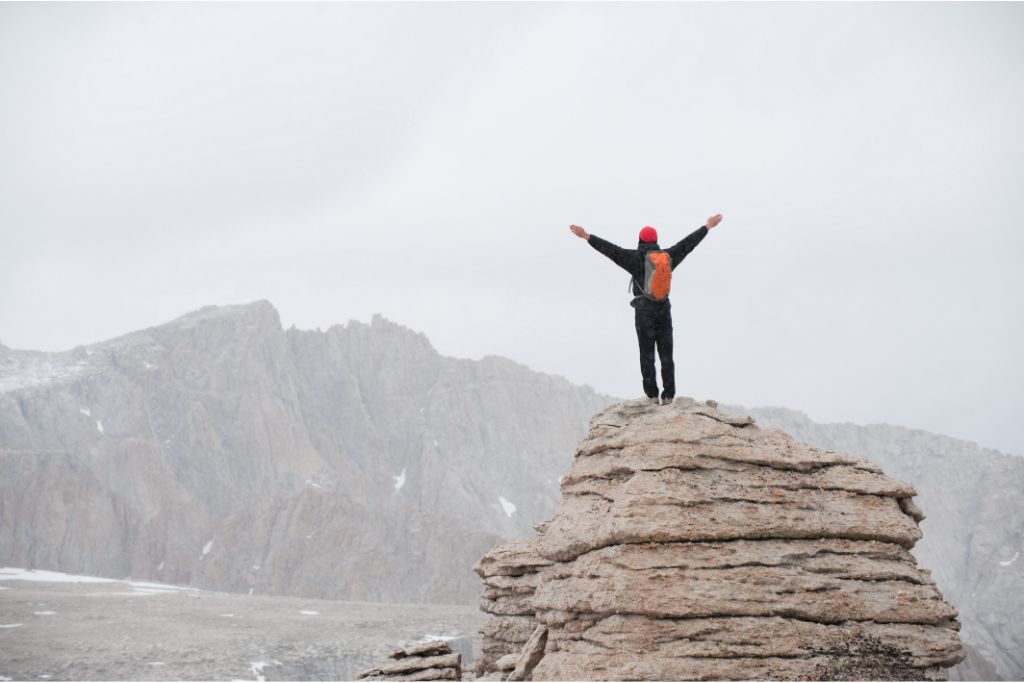 man lifting his arms while standing at the top of a rock