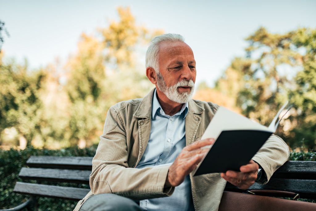 An Old man is reading a book in nature.