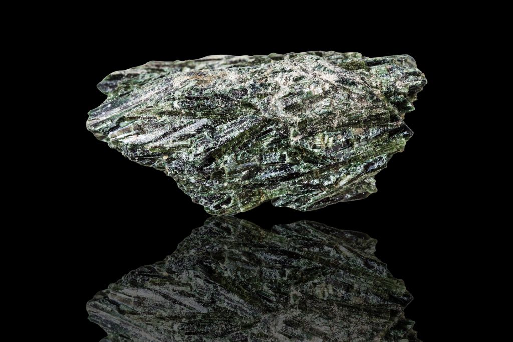 A raw Actinolite crystal on a black reflective background
