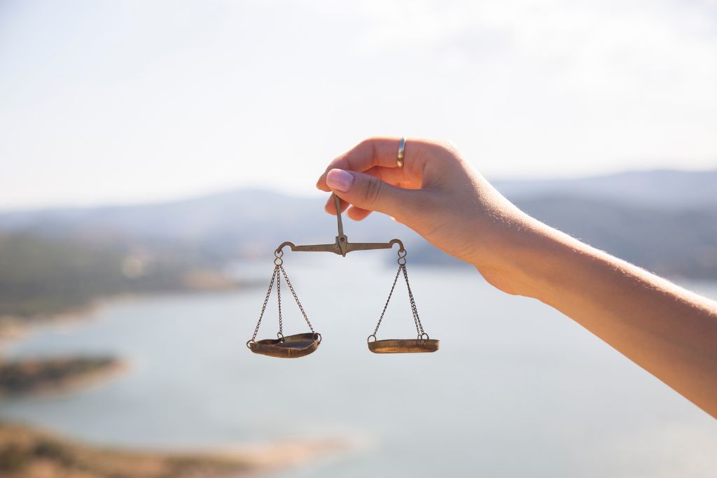 a hand holding a balancing scale with the view of the ocean