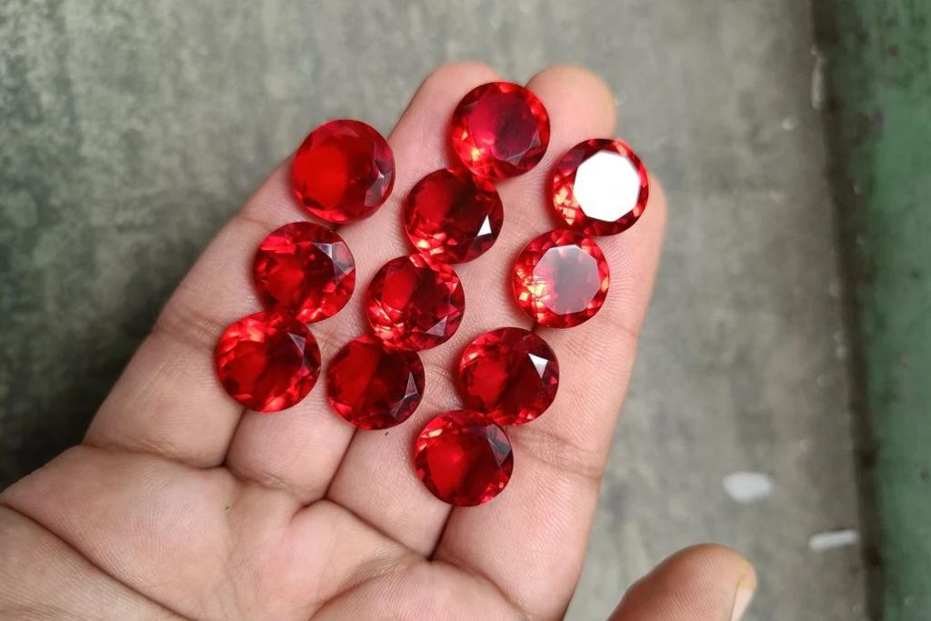 a hand holding 11 pieces of round shaped Red Diamond on a concrete background