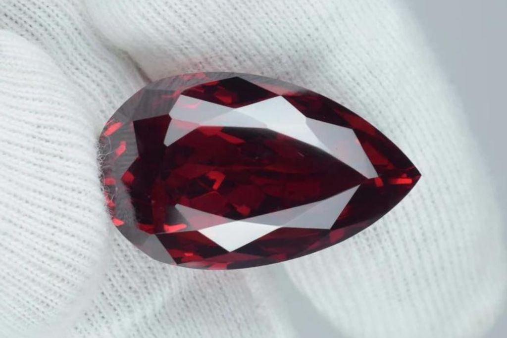 A gloved hand holding a polished teardrop shaped Red Zircon